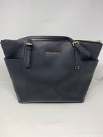 Front view of black Michael Kors tote bag showing gold tone logo and handles.