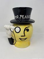 Front view of vintage Planters Mr. Peanut ceramic cookie jar with black top hat lid showing white raised lettering and monocle detail.