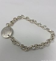 Full view of bracelet showing cable link chain and round tag on white background