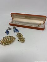 Full view of jewelry lot including Napier pearl necklace in orange box, blue and clear rhinestone earrings, yellow rhinestone brooch and matching earrings.