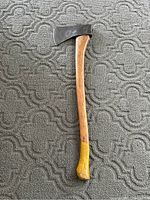 Full view of vintage wooden handled axe with yellow paint on the handle's end and metal axe head.