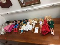 Nine Barbie dolls lying on a wooden surface, showcasing various different outfits and hair styles.