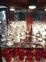 Photo of 4 etched large water glasses and 5 wine glasses with frosted tulip design on a glass shelf, reflected by a mirror.