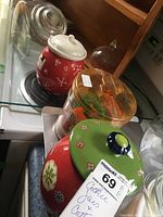 Photo showing two red ceramic cookie jars and one clear plastic cookie jar with assorted cookie cutters inside.