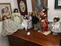 Lot of six decorative dolls arranged on wooden surface including porcelain and cultural dolls with varied costumes.