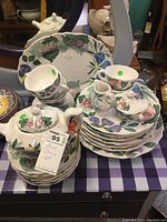 Photo of floral china set stacked showing multiple plates, cups, saucers, creamer, sugar bowl with lid, featuring grape leaves and colorful floral pattern