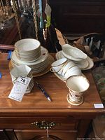 Full display of the china pieces including plates, bowls, cups, and a goblet on a wooden surface.