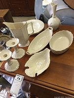 Photo showing seven white Lenox porcelain pieces including candle holders, pitchers, platters, vase, and bowl on a wooden table.