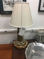 Full view of the lighthouse style table lamp showing the cylindrical body, rope wrapped base, pleated cream-colored lampshade, electrical cord coiled at base.