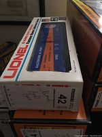 Lionel O gauge Baltimore & Ohio box car visible through original box window, showing blue and orange coloring and branding.