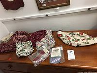 Photo showing six fabric liners spread on a wooden surface. Patterns include dark red floral, white with strawberries, multi-colored floral, and tartan plaid. Some liners packaged.