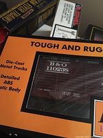 Close-up of orange box with window showing brown B&O stock car model with die-cast metal trucks and details about plastic body.