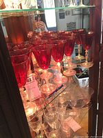 Set of 12 red stemmed glasses displayed on mirrored shelf, showing entire set and reflection, confirming 12 glasses.
