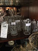 Photo showing multiple (10) clear glass tumblers with etched ship and 'Remember The Maine' wording on a shelf.