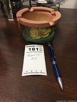 Full view of the round ceramic Roseville Pottery ashtray Mold 27 with floral design, next to pen and tag for size reference.