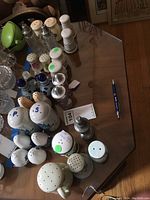 Photo of large assortment of salt and pepper shakers on a wooden table showing various styles and materials from ceramic to glass.