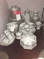 Stack of plates, bowls, cups, a coffee pot, and a covered dish with blue floral and gold trim pattern seen on all pieces