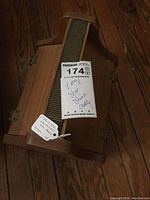 Closed vintage wooden shoe shine caddy showing curved handle and metal side hinges, placed on wooden floor.