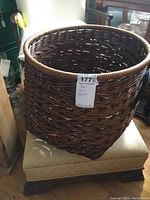 Photo showing large round woven basket with handles placed on a beige cushioned seat.