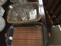 Eight clear glass tumblers inside a woven basket and a rectangular clear glass baking dish underneath