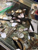 Mixed lot of wristwatches showing various styles and types on a glass surface with price tag.