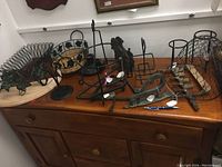 Overview of assorted black wrought iron decorative and functional items on a wooden table including trays, holders, hooks and decorative baskets