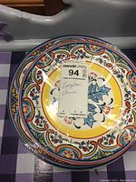 Top view of stacked colorful Zanzibar China dinner plates showing floral and scroll patterns with yellow centers and border details.