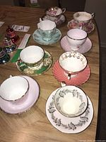 Photo showing eight assorted cups and saucers with colorful patterns and gold trim on a wooden table