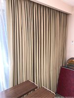 Lined beige/tan pleated curtains closed, with some sheer curtains visible behind.