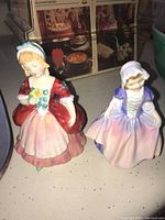 Front view of two Royal Doulton figurines, one in red and pink dress, the other in purple and lavender dress.