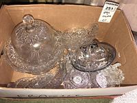 Box of assorted glass and crystal serving dishes with a cake dome, large serving bowl, trays, and small dishes.