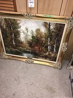 Full view of the oil painting resting against a wall showing the entire artwork and ornate gold frame.