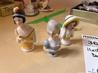 Overview of three antique porcelain pin cushion half dolls showing variations in hairstyle, attire, and size.