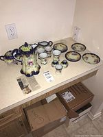 Full coffee set including pot, cups, plates, cream and sugar holders, and salt and pepper shakers arranged on a counter surface.