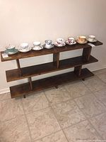 Front view of wood open shelving unit holding seven decorative teacup and saucer sets on top shelf