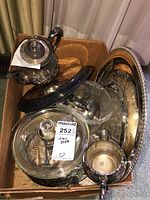 Photo showing multiple pieces of silver plated servingware including a teapot, covered dish, sugar bowl, and trays in a cardboard box.