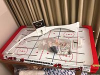 Overview of tabletop hockey game board showing playing surface, goals, and player figures in plastic bags.