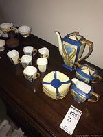 Overall view of the complete tea set, showing six cups, six saucers, teapot, sugar and milk containers on wooden surface.