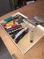 Image showing HO scale train cars including a green boxcar, yellow car, burgundy passenger car and a black locomotive, along with train accessories and booklets in a box.