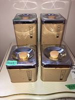 Four vintage Lincoln Beautyware metal canisters with chrome lids and wooden knobs, arranged in a group showing wear and scratches.