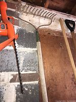 Orange electric chainsaw leaning against cinder block wall with a garden rake and shovel visible