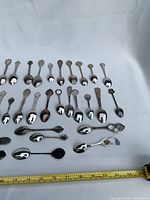 Group of souvenir spoons laid out with ruler for scale
