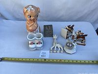 Front view of all seven items including piglet, coin bank, planter, teether and deer figurines with measuring tape for scale