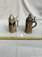 Both steins side by side with measuring tape for scale