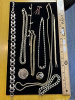 Full lot overview showing all gold-tone jewellery pieces on black board beside ruler