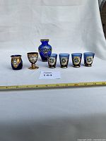 All seven cobalt blue glass pieces lined up: vase, goblet, tumbler, four shot glasses