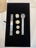 Five wristwatches arrayed with ruler for scale