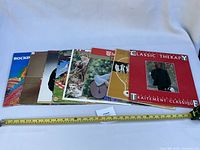 All ten records overlapped showing spine widths and front cover artwork with measuring tape for scale