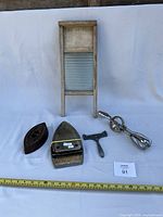 Group shot showing all five items: washboard, sad iron base, iron rest, egg beater, peeler