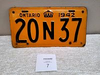 Front view of 1942 Ontario metal license plate showing orange background with black embossed text, crown symbol, and license number '20N 37'. Plate rests on a white textured surface.